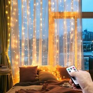 a person holding a remote control in front of a window with fairy lights on it