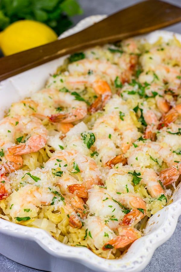 a casserole dish with shrimp and pasta in it next to lemon wedges