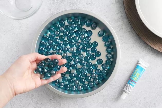 a bowl filled with blue beads next to a bottle of toothpaste and a glass of water