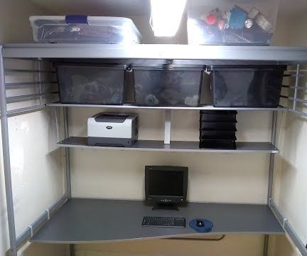 a computer desk in the corner of a room with shelves and bins on it