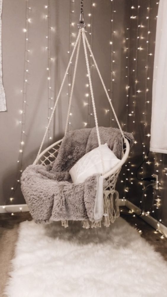 a hanging chair with some lights on the wall behind it and a rug in front of it