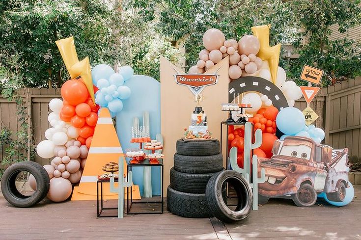 an assortment of balloons and decorations on display in front of a car themed birthday party