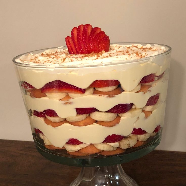 a layered cake with strawberries and whipped cream in a glass dish on a wooden table