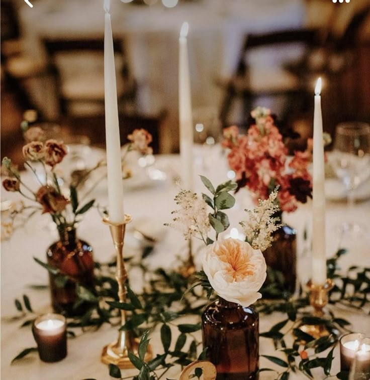 a table topped with candles and flowers on top of a white table cloth covered in greenery