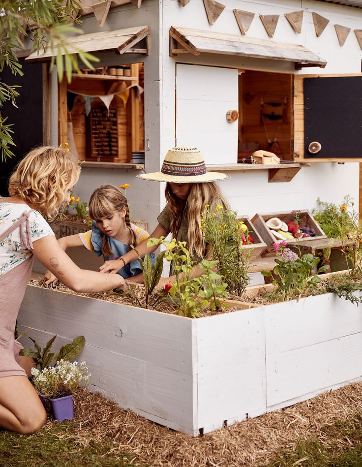 two women and a child are working in a raised garden bed that is built into the side of a house