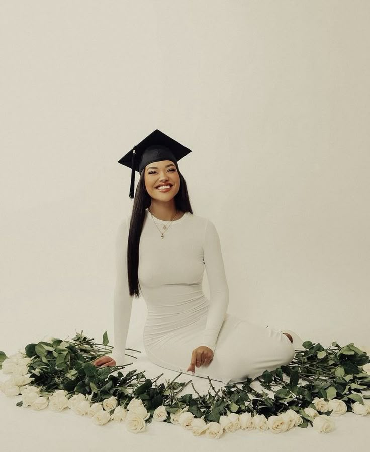 a woman wearing a graduation cap sitting on the ground with flowers around her and smiling