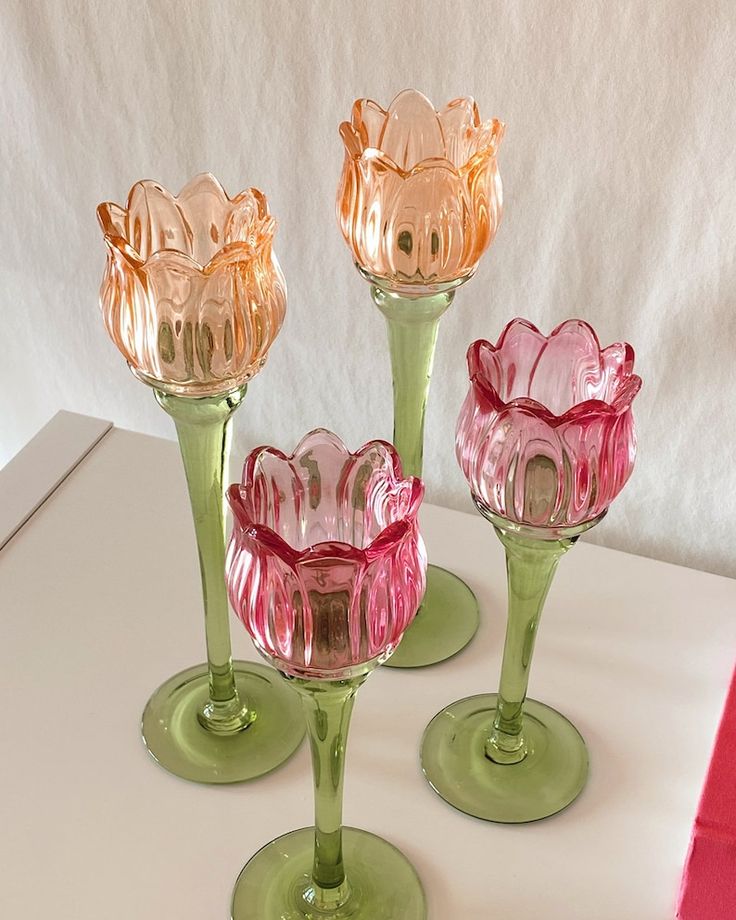 three pink and green glass vases sitting on top of a white table next to each other