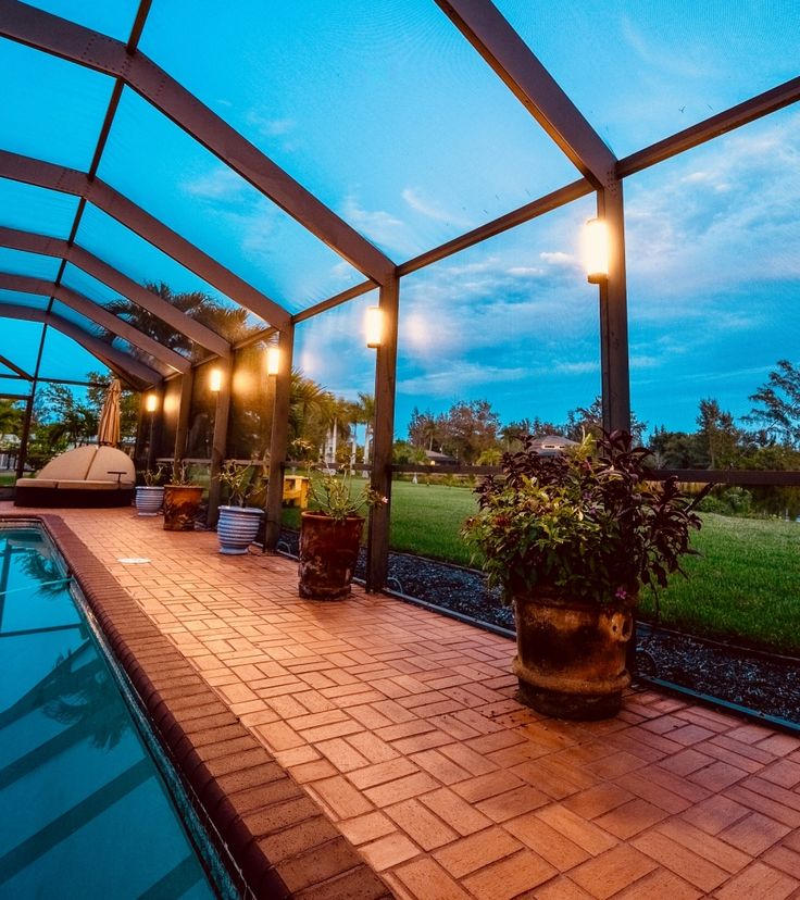 an outdoor swimming pool with potted plants and lights on the side of it at dusk