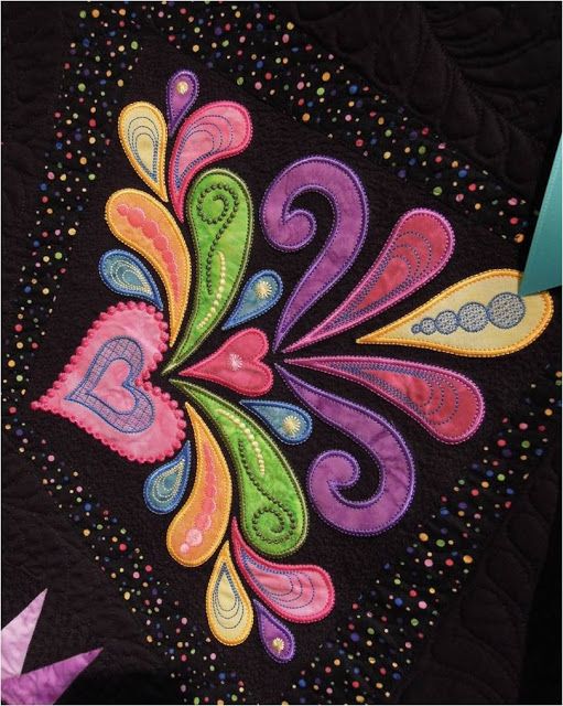 a close up of a colorful quilt on a black table cloth with the letter b in it