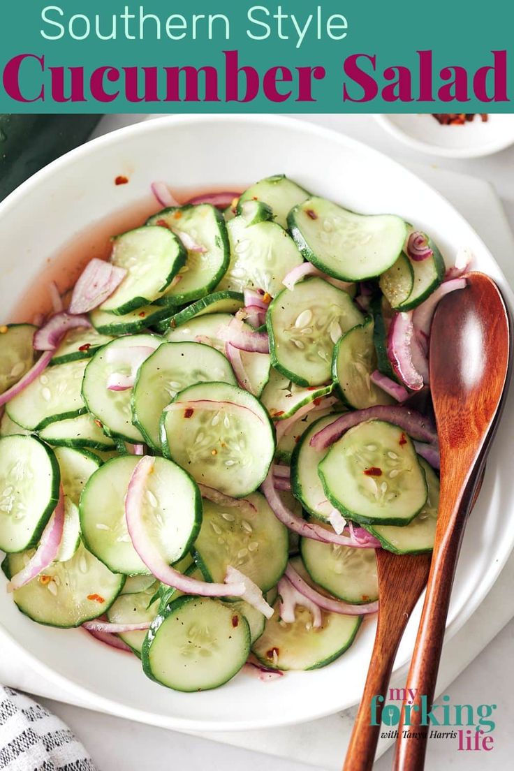 a white bowl filled with cucumber salad next to a wooden spoon on top of a table