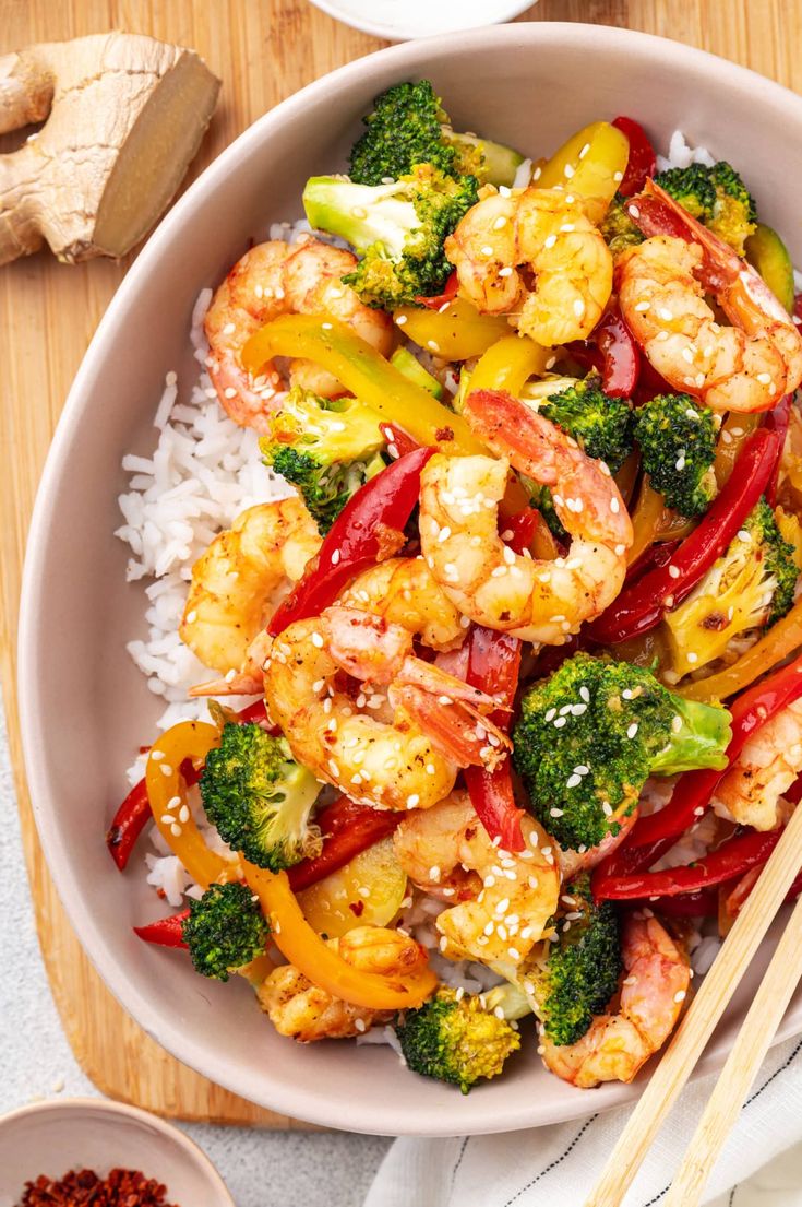 shrimp, broccoli and peppers served on rice in a bowl with chopsticks