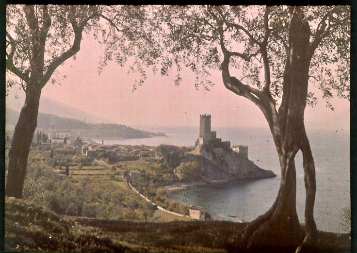 an old photo of a castle in the middle of trees and water with mountains in the background