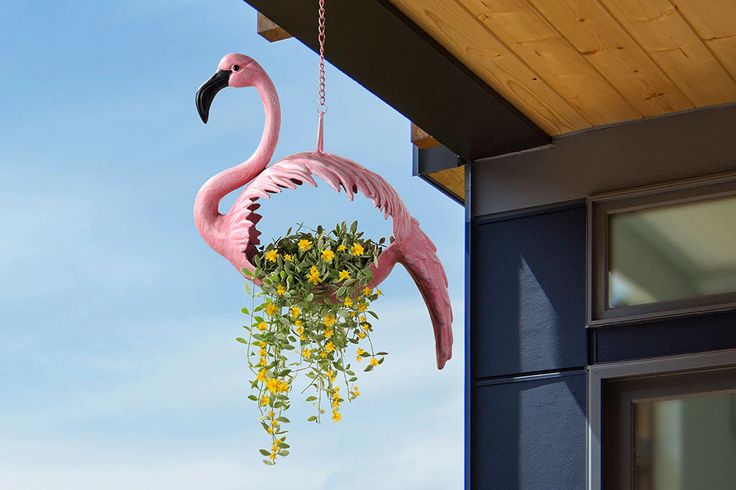 a pink flamingo hanging from the side of a building with flowers in its beak