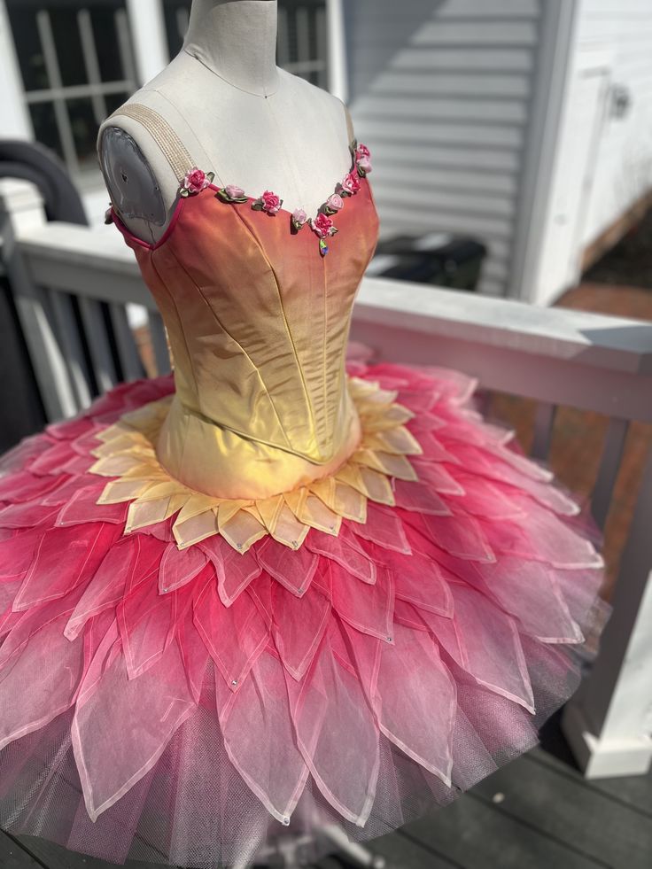 a dress made out of tulle with pink and yellow flowers on the bottom, sitting on a wooden deck