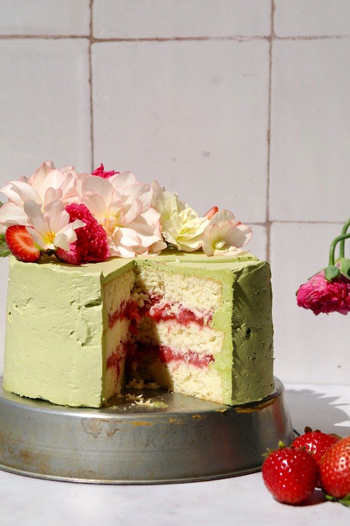 a green cake with flowers and strawberries on the side