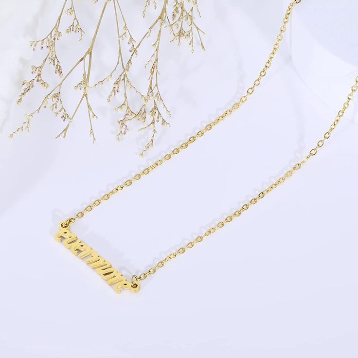 a gold necklace with the word mom written in cursive writing on it, sitting next to some branches