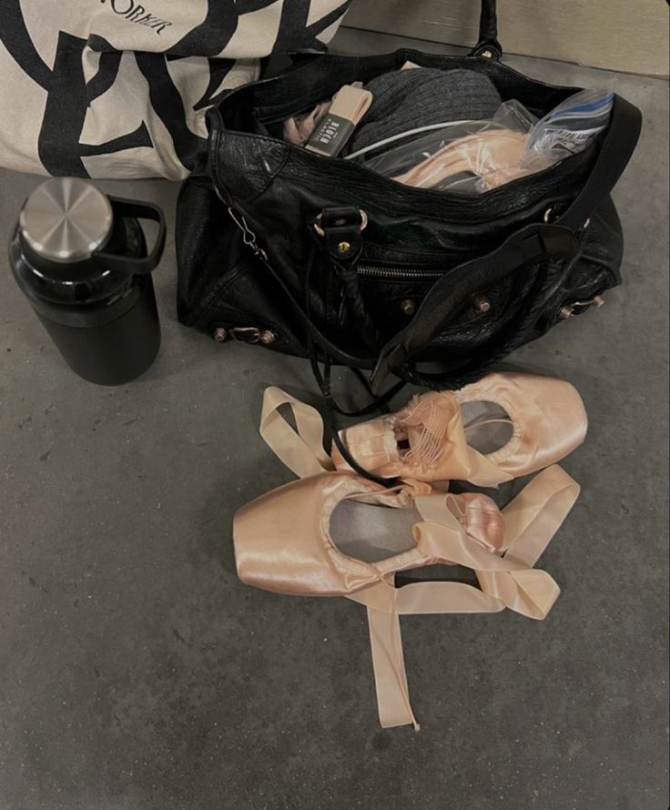 an open black bag sitting on the ground next to ballet shoes