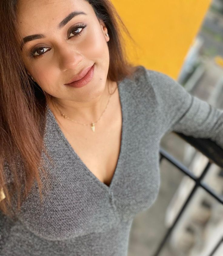 a woman with brown hair is posing for the camera while wearing a gray sweater and gold necklace