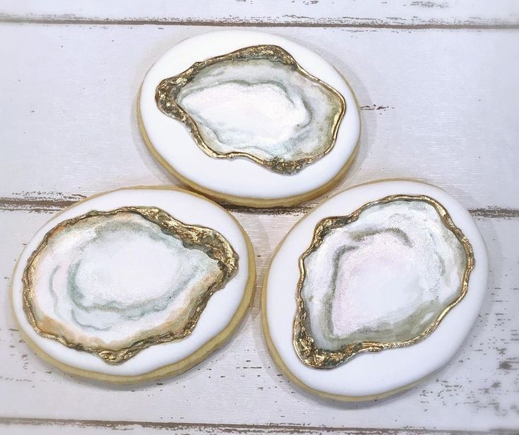 three white and gold decorated cookies sitting on top of a wooden table next to each other