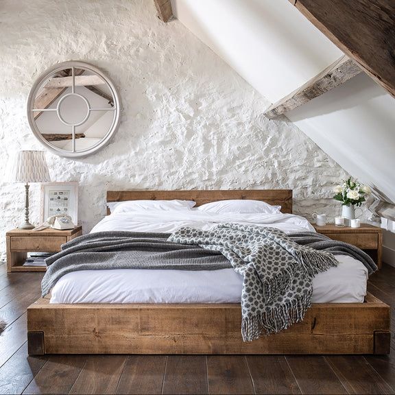 a bed sitting in the middle of a bedroom next to a white wall and wooden floor