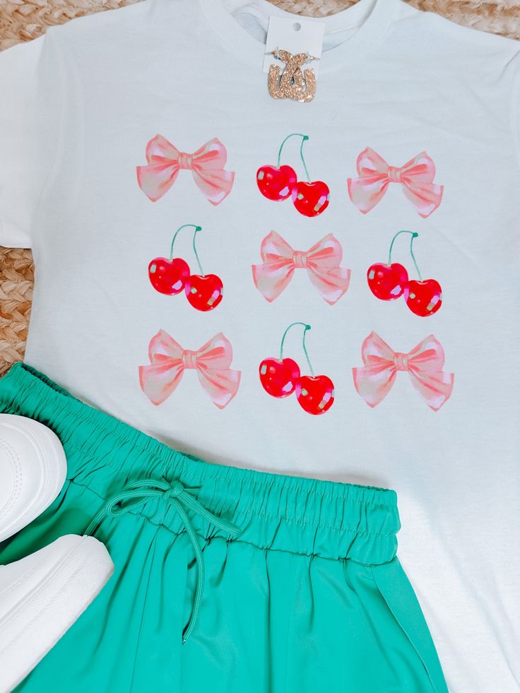 This super soft white graphic tee features a playful grid of cherries and pink bows. Perfect for adding a pop of whimsy to your wardrobe, this tee is available in sizes S-2XL. Embrace your inner cherry lover and make a statement with this fun and stylish piece! Spring Cotton T-shirt With Bow, Cute Bow T-shirt For Spring, Sweet Style T-shirt With Funny Print For Spring, Cute Spring T-shirt With Sublimation Print, Playful Tops With Sublimation Print For Summer, Cute Pink Tops With Sublimation Print, Pink Cute Top With Sublimation Print, Cute White Top With Cherry Print, Cute Pink T-shirt With Cherry Print