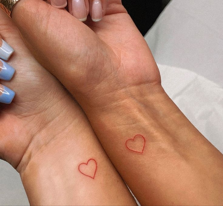 two people with matching tattoos on their arms holding each other's hands and looking at the camera