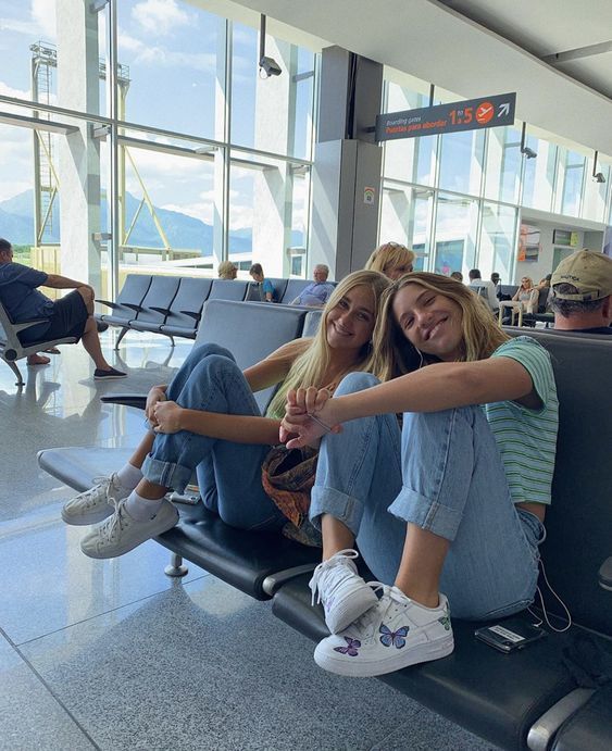 two young women sitting on the back of an airport luggage cart smiling at the camera