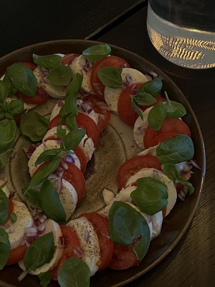 a plate with sliced tomatoes, mozzarella and spinach on it next to a glass of water