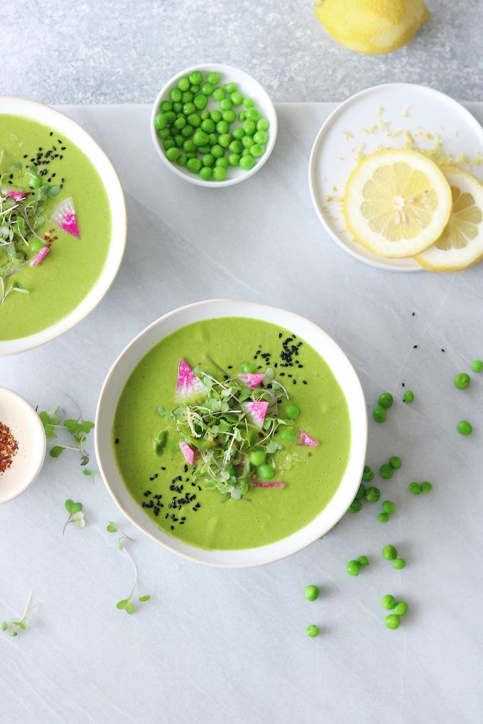 three bowls filled with green pea soup next to lemon slices and peas on a table