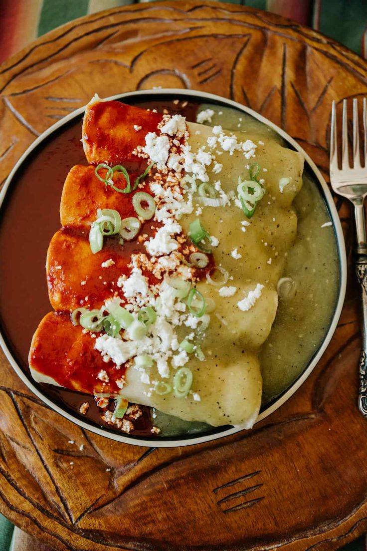 a plate with ravioli, cheese and green onions on it next to a fork