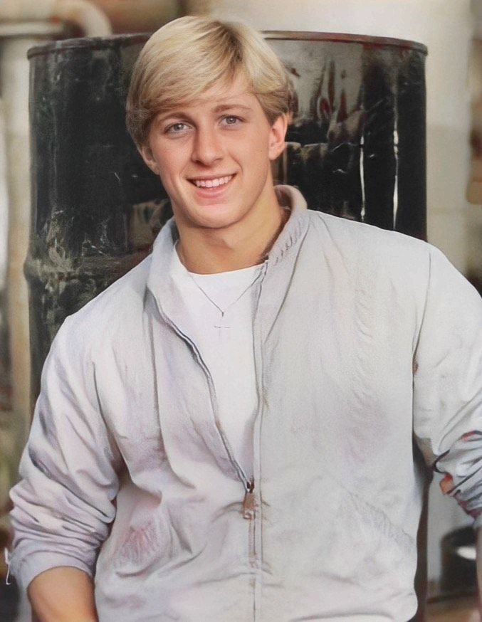 a young man with blonde hair wearing a white shirt and black pants is smiling at the camera