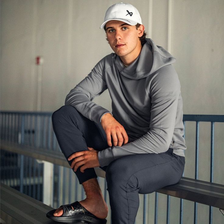 a man sitting on top of a metal bench wearing a white hat and gray shirt