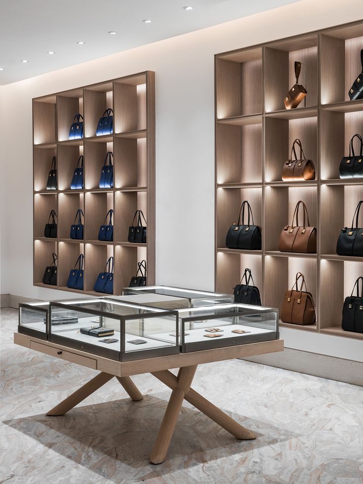 a display case with many purses and handbags on shelves in a room filled with wooden shelving