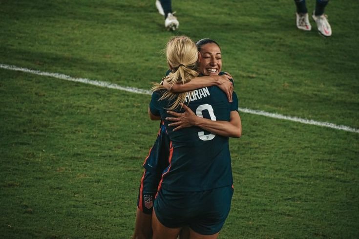 two female soccer players hugging each other on the field