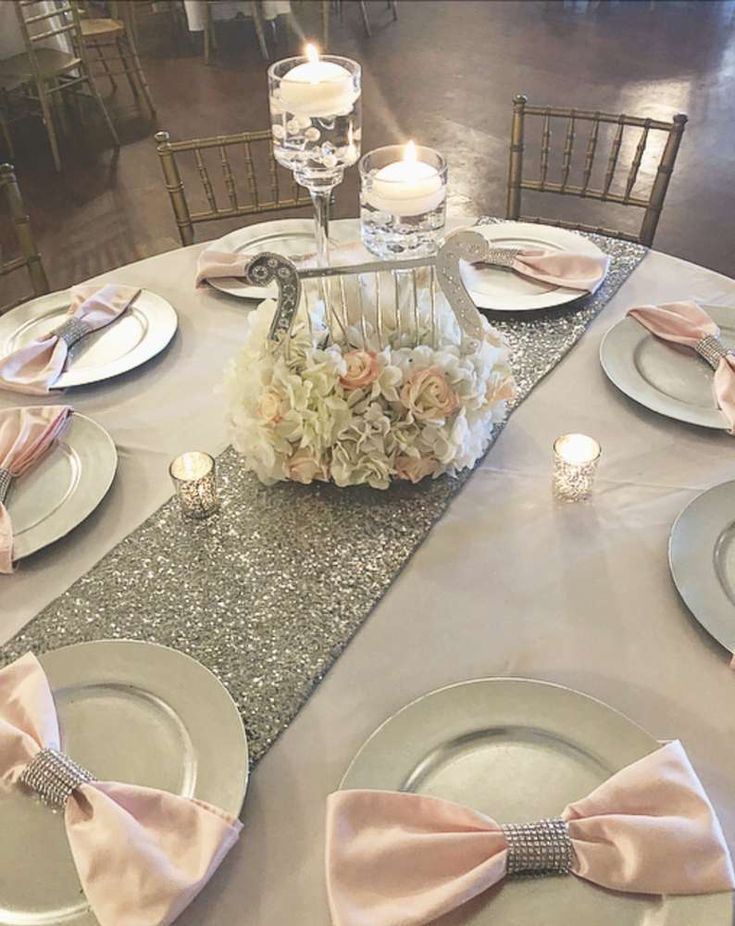 the table is set with silver and white plates, pink napkins, and centerpieces