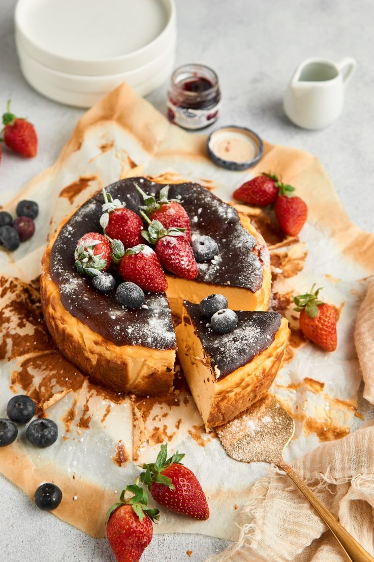 a chocolate cake with strawberries and blueberries on top, surrounded by other dessert items