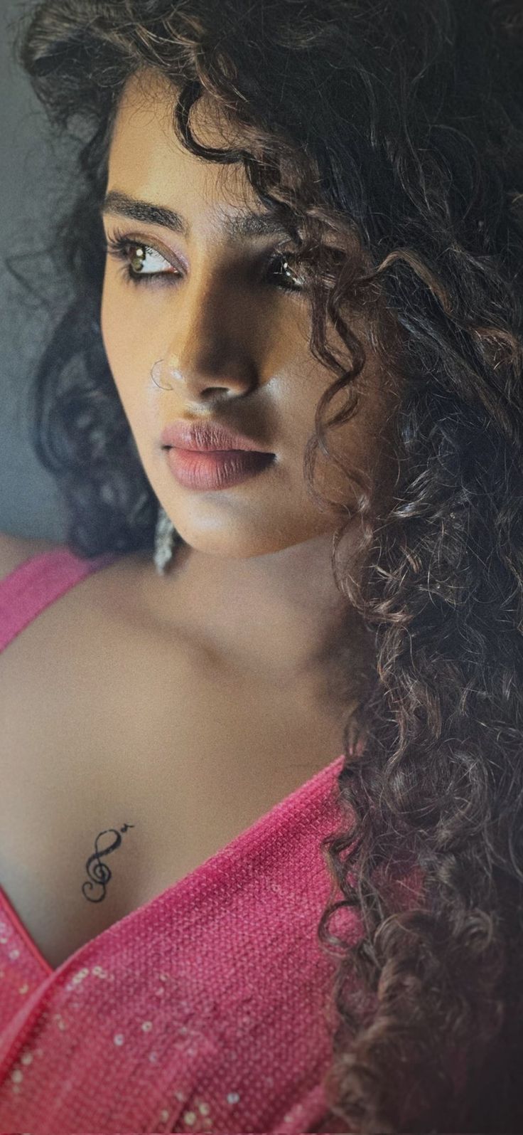 a close up of a person wearing a pink shirt with curly hair and tattoos on her chest