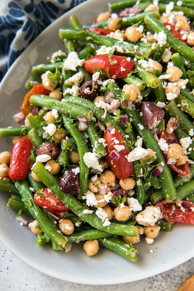 a white plate topped with green beans, tomatoes and feta cheese on top of it