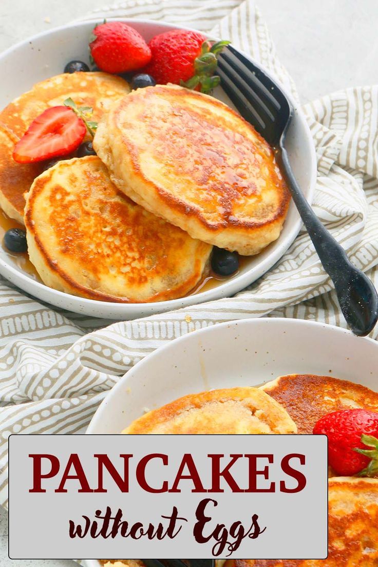 pancakes with strawberries and blueberries in a white bowl next to a fork on a striped cloth