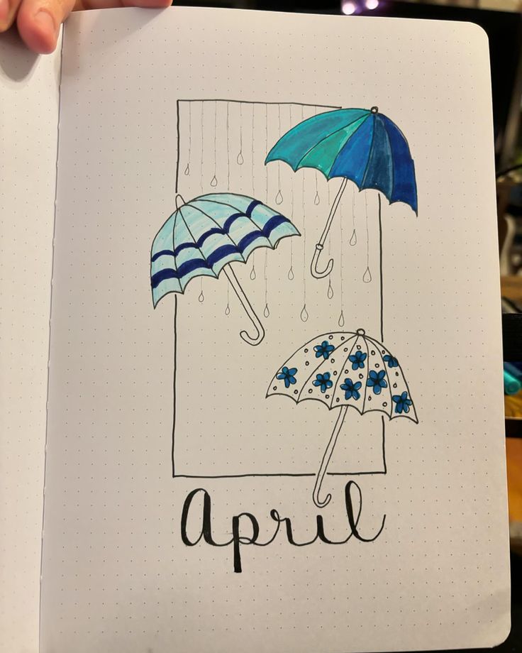 an open notebook with two umbrellas and the word april written in black on it