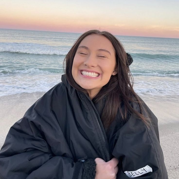 a woman standing on top of a sandy beach next to the ocean with her eyes closed