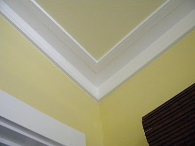 the corner of a room with yellow walls and white trim on the ceiling is shown