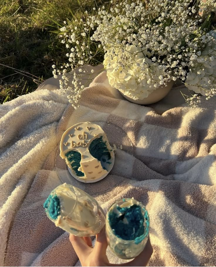 someone is holding their hand up to some cupcakes on a blanket with flowers in the background