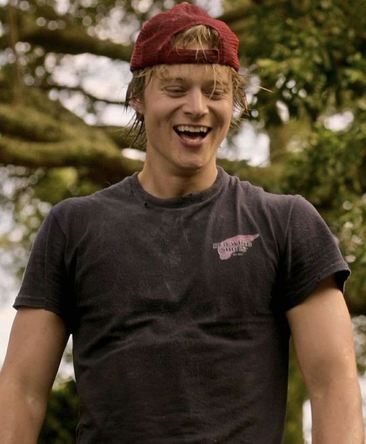 a young man is laughing and holding a frisbee in his hand while wearing a red hat