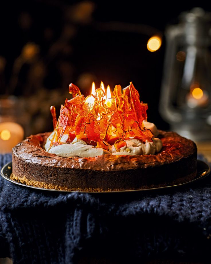 a cake with orange frosting and candles on it sitting on a table in front of some lit candles