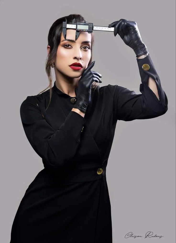 a woman in black dress and gloves holding a pair of scissors over her head with both hands