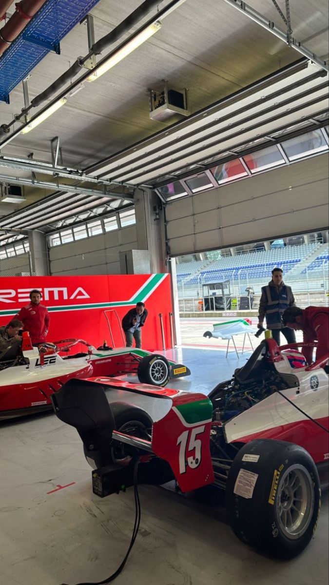 two racing cars are parked in a garage with people standing around them and looking on