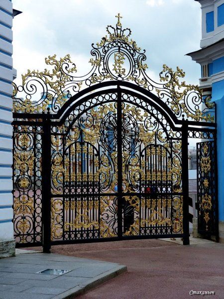 an ornate iron gate with gold designs on it's sides in front of a blue and white building