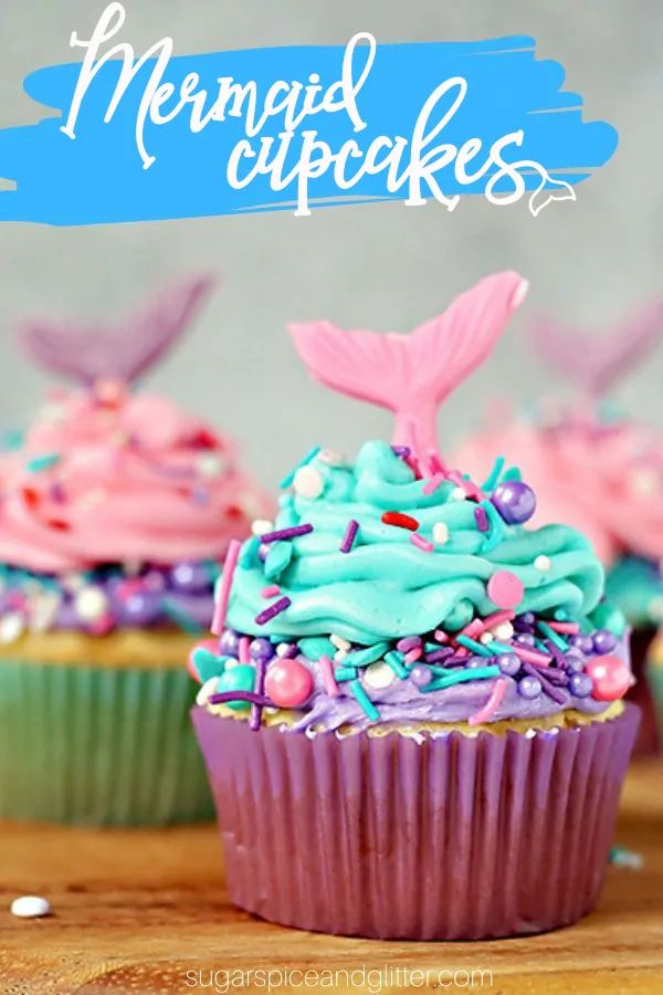 mermaid cupcakes with sprinkles and blue frosting on top are sitting on a wooden table