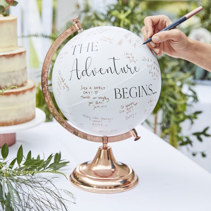 a person is writing on a globe at a table with flowers and greenery in the background